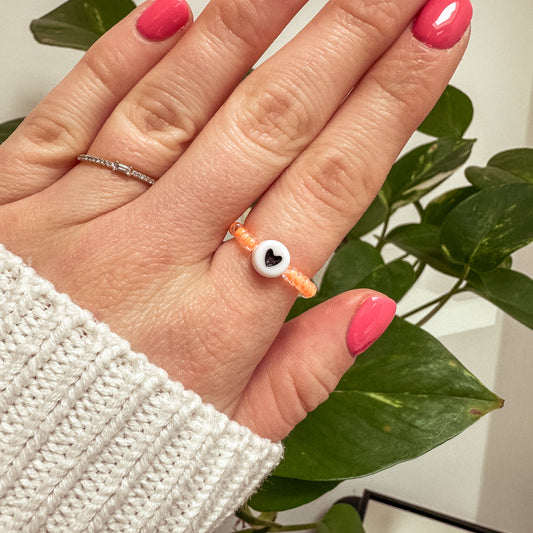 Perlenring aus orangenen Glasperlen mit Herz in Schwarz